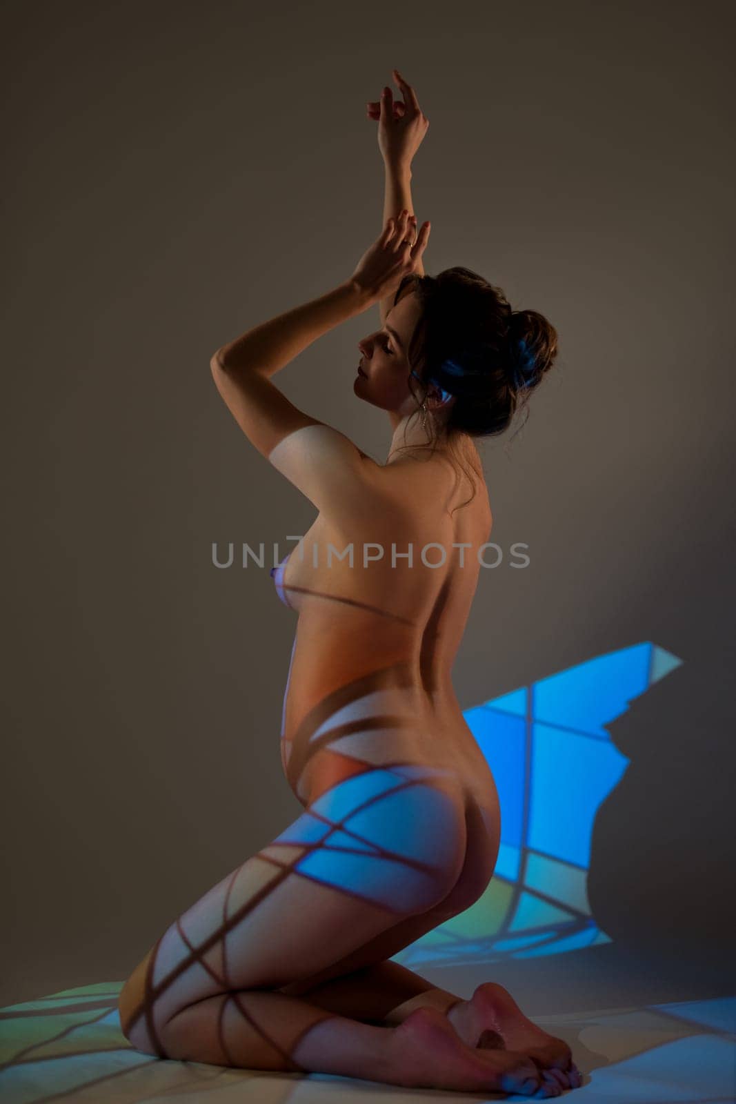 Side view of naked pregnant female sitting with closed eyes on floor in dark studio with blue neon light