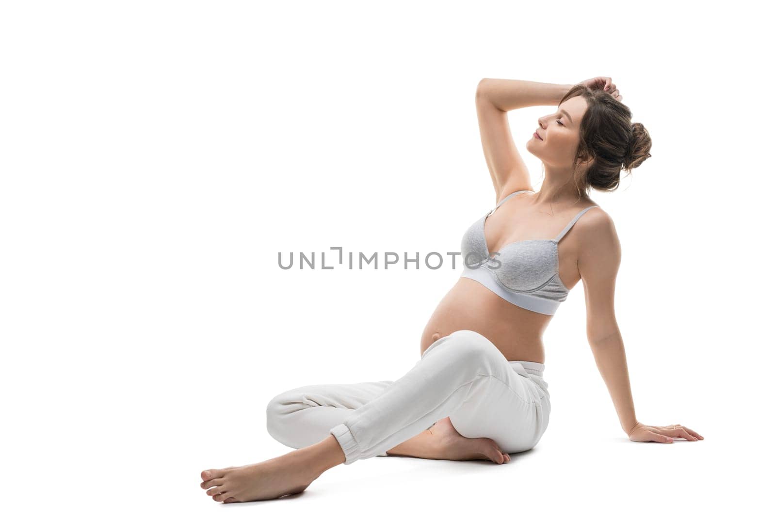 Full body side view of sensual gentle young pregnant female in white lingerie relax after stretching gracefully against white background isolated