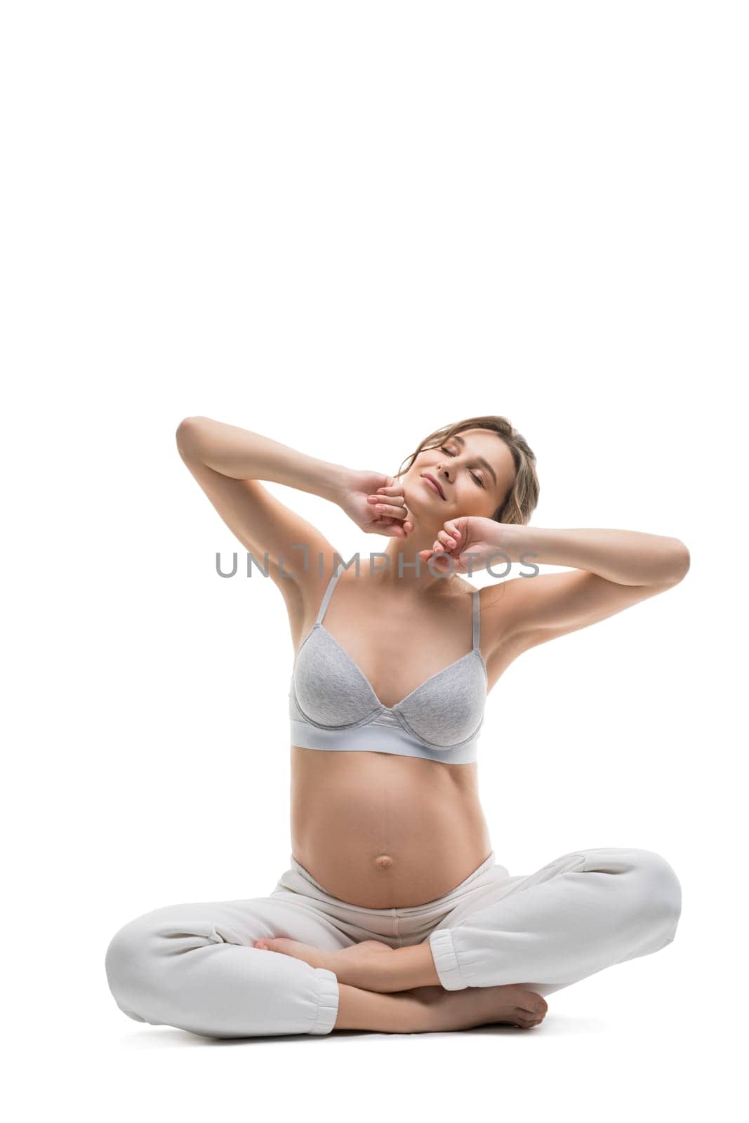 Full body side view of sensual gentle young pregnant female in white lingerie relax after stretching gracefully against white background isolated