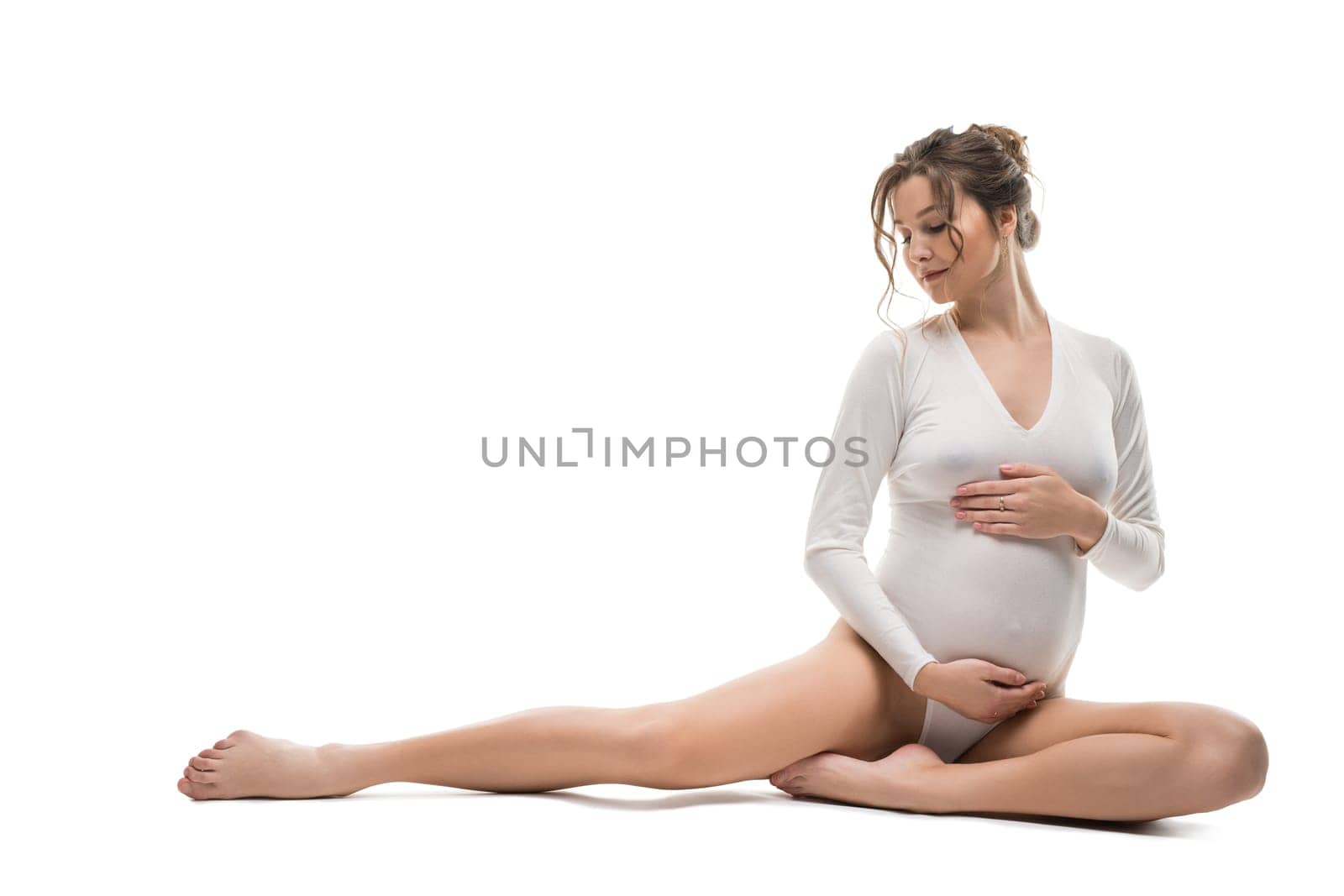 Full body side view of sensual gentle young pregnant female in white bodysuit relax after stretching gracefully against white background