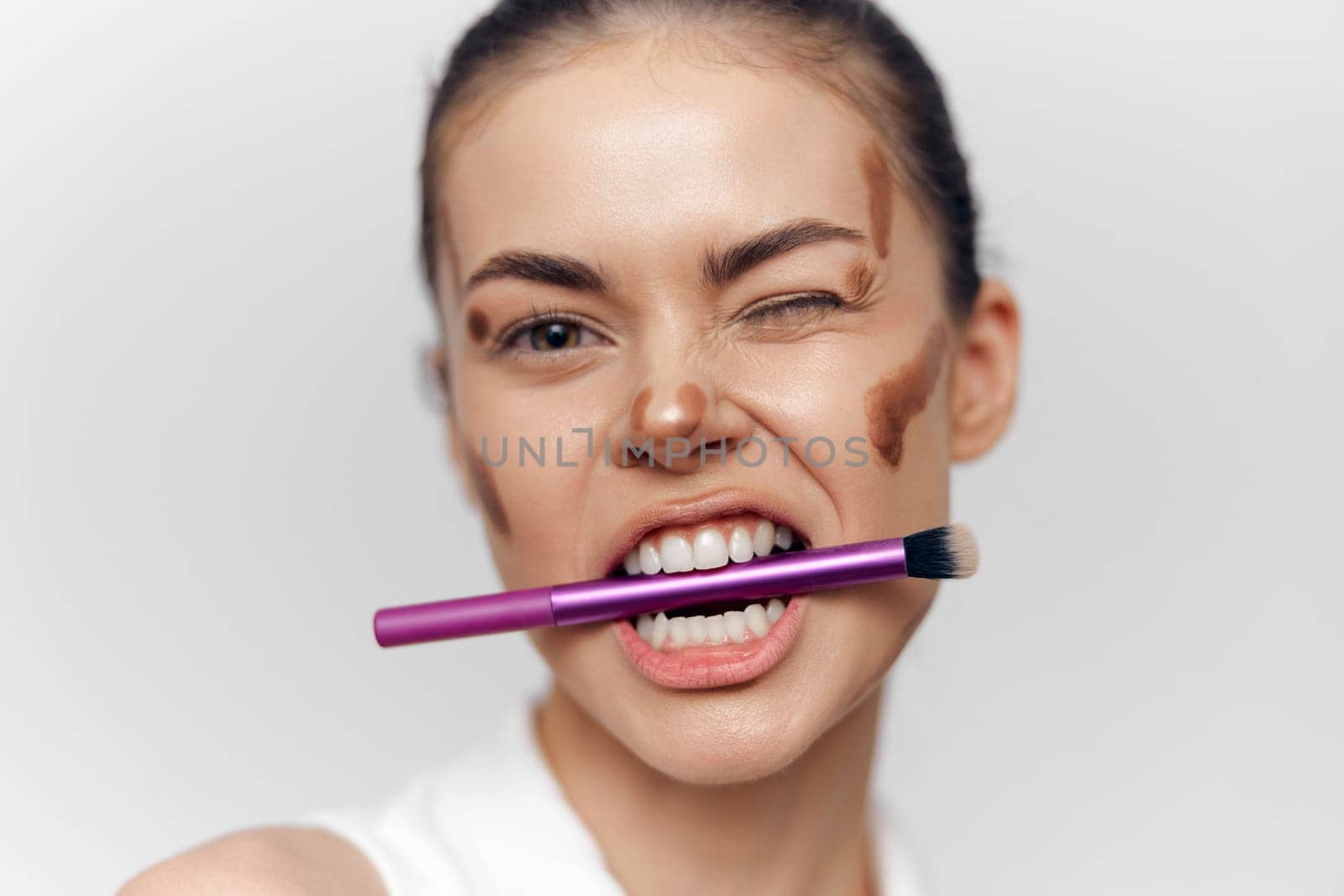 A young model demonstrates confidence and fun while applying makeup with a brush, featuring joyful expression and artistic elegance in a clean white background.