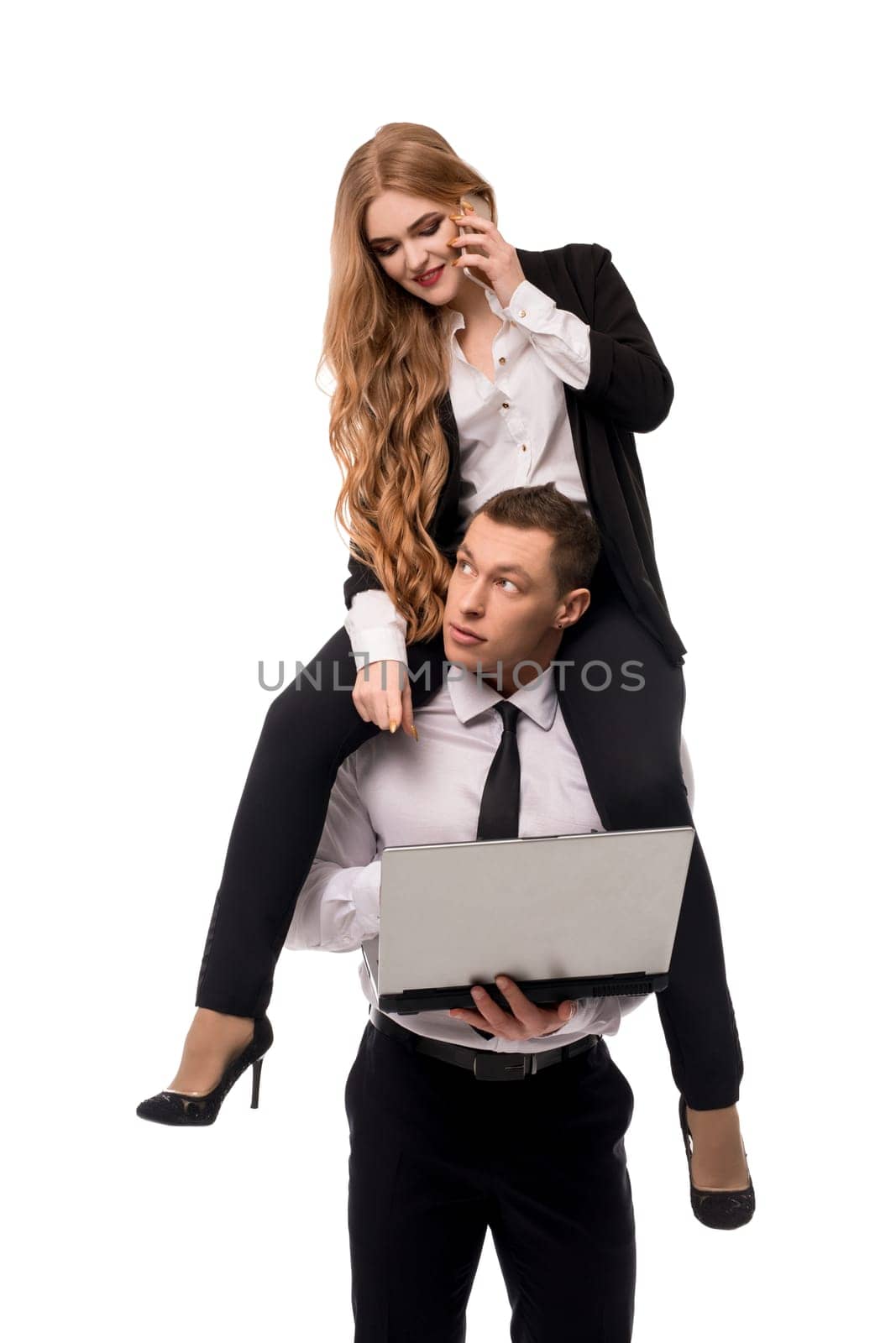 Businesswoman in formal wear speaking on smartphone while sitting on shoulders of businessman using laptop isolated on white background