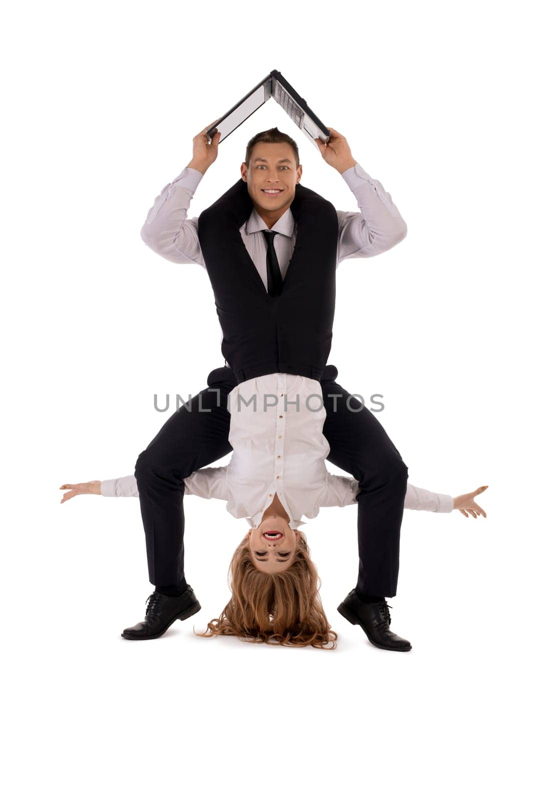 Happy businesswoman hanging upside down on neck of cheerful businessman with laptop isolated on white background