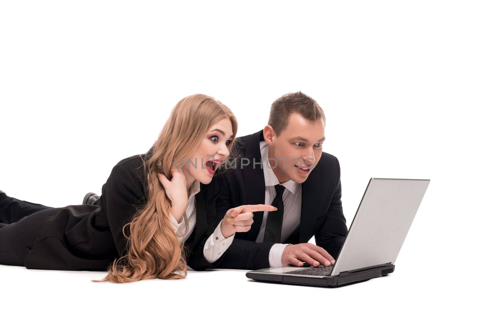 Excited businesswoman in suit pointing at screen of laptop while lying near colleague against white background