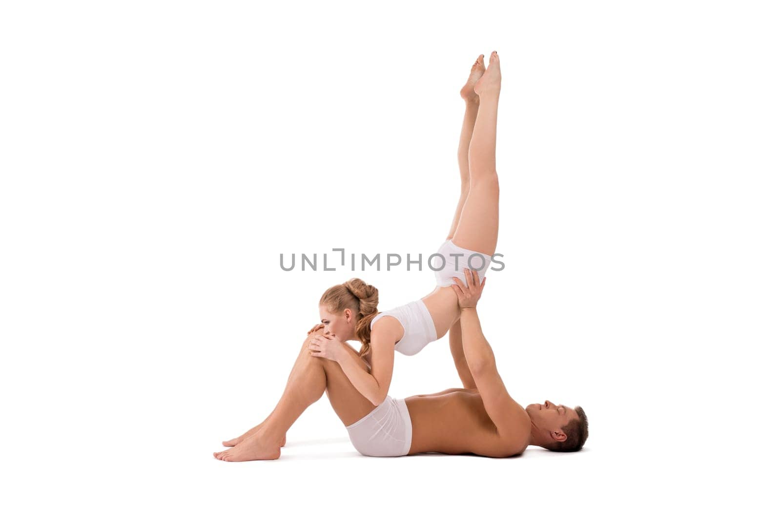 Side view of shirtless man supporting slim woman in underwear while doing gymnastic against white background