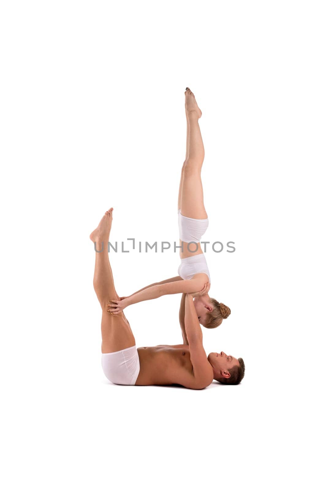 Full body side view of flexible young man and woman in white underwear doing acro yoga against white background