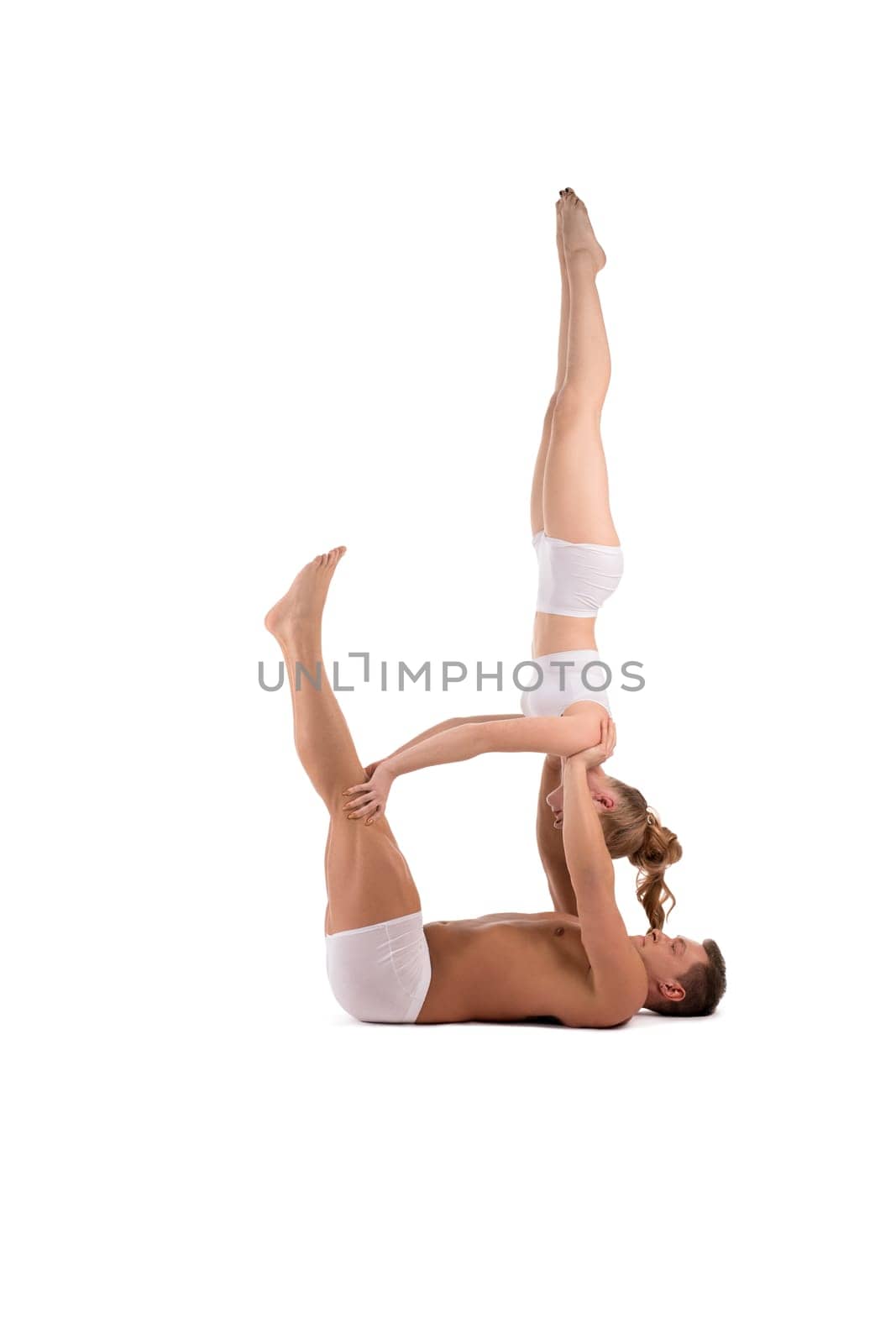 Full body side view of flexible young man and woman in white underwear doing acro yoga against white background