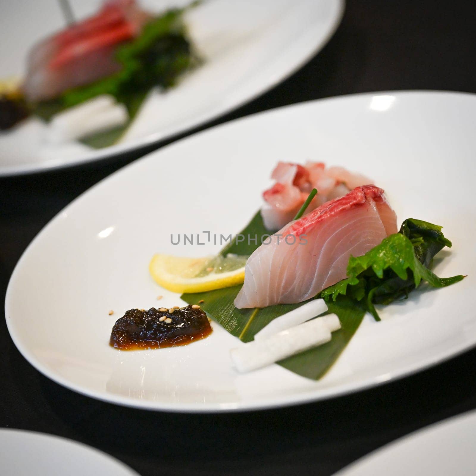 Sliced fish is artfully placed on a bed of greens, garnished with fresh lemon and a rich sauce, showcasing the elegance of Japanese culinary presentation.