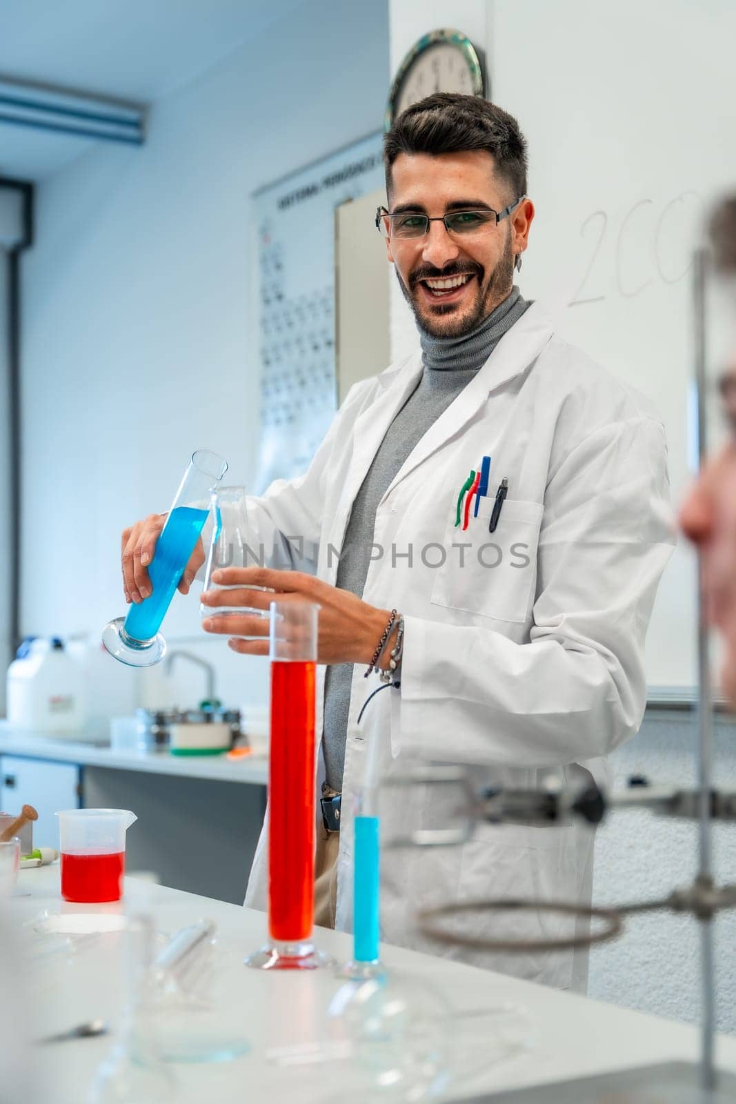 Young male scientist pouring blue liquid into laboratory glassware while smiling during an experiment in a university or school lab