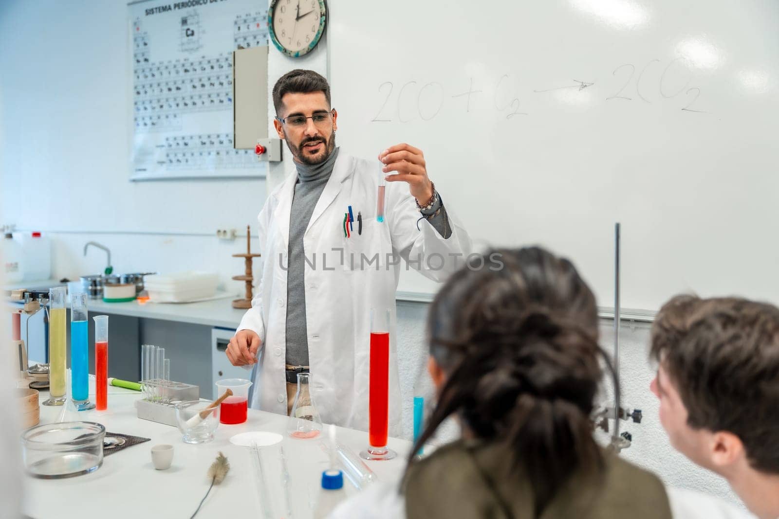 Chemistry teacher showing test tube with chemical reaction to students during experiment in university laboratory