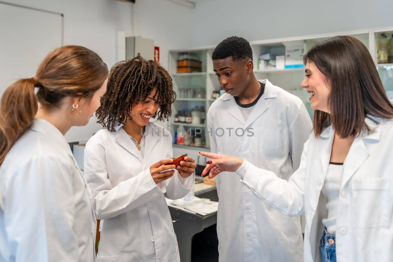 Group of diverse university students wearing lab coats examining a specimen during a scientific experiment in a laboratory
