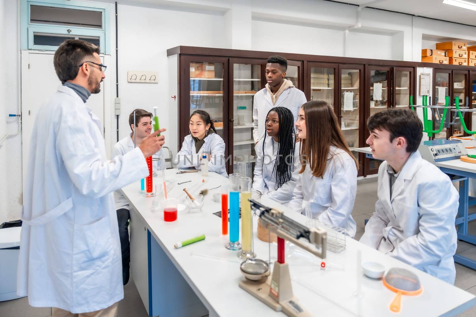 Chemistry teacher holding a test tube and explaining experiment to students sitting at desk in university laboratory
