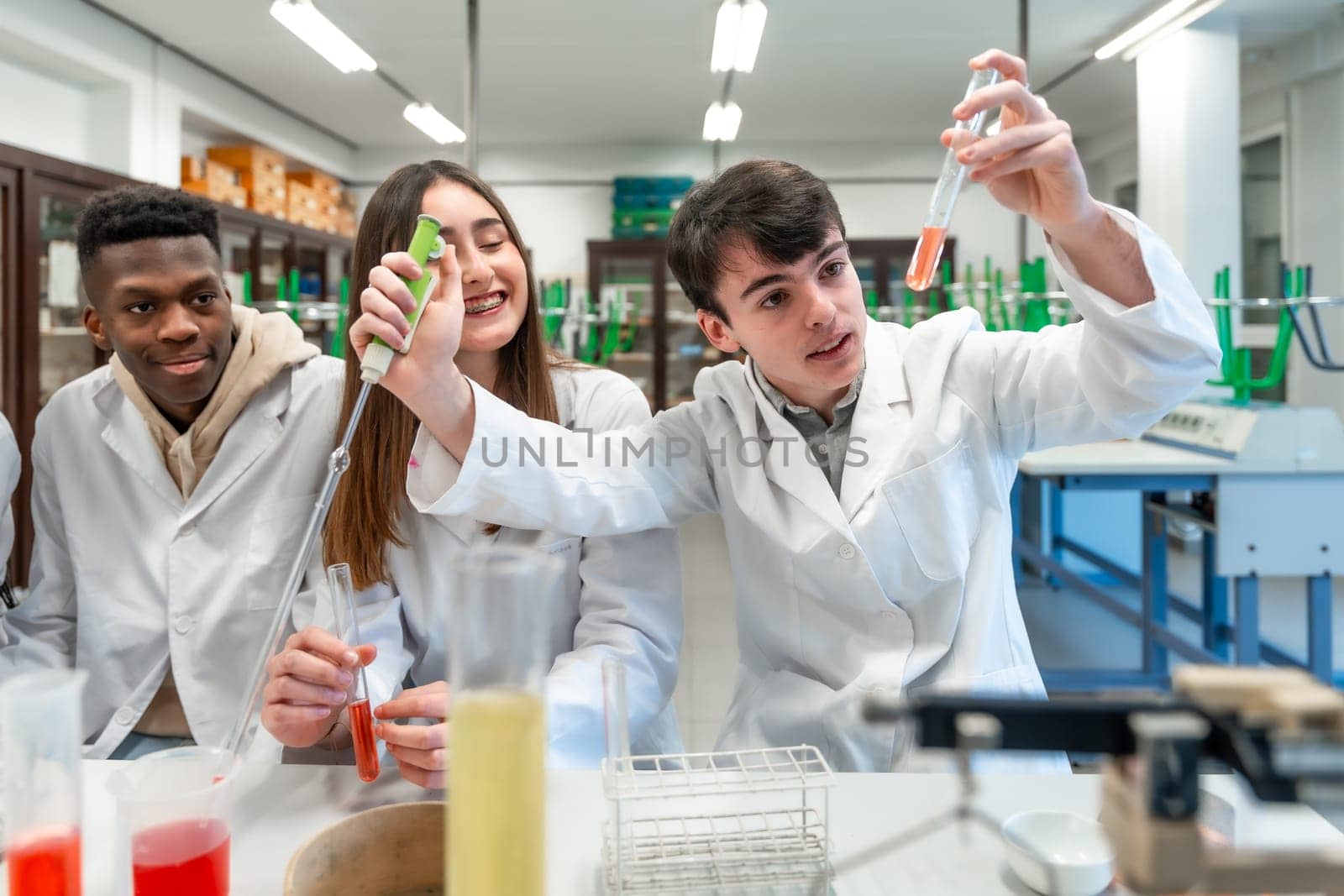 Young chemistry students wearing lab coats performing experiment using test tubes and other laboratory equipment