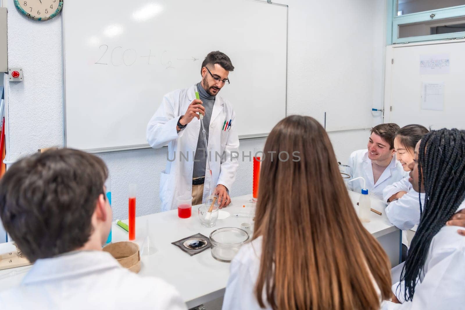 Chemistry teacher performing a chemical experiment with students in a university laboratory, using lab coats and equipment