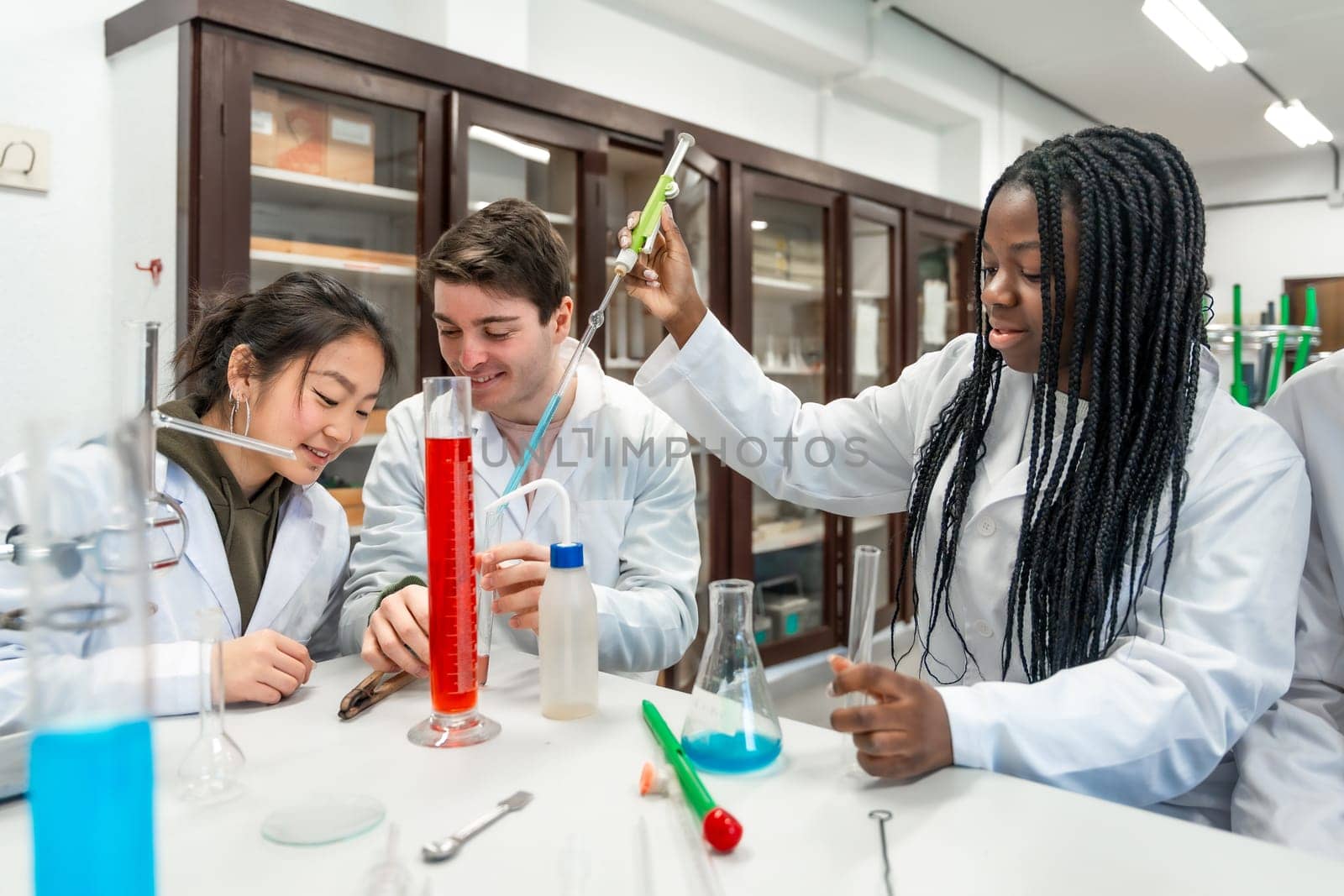 Multi ethnic university students wearing lab coats conducting a chemistry experiment using colorful liquids and lab equipment