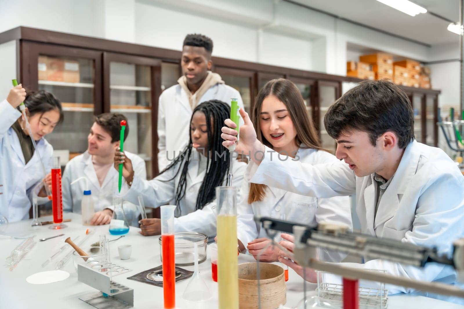 Multi ethnic university students wearing lab coats conducting a chemistry experiment using test tubes and beakers in a science laboratory