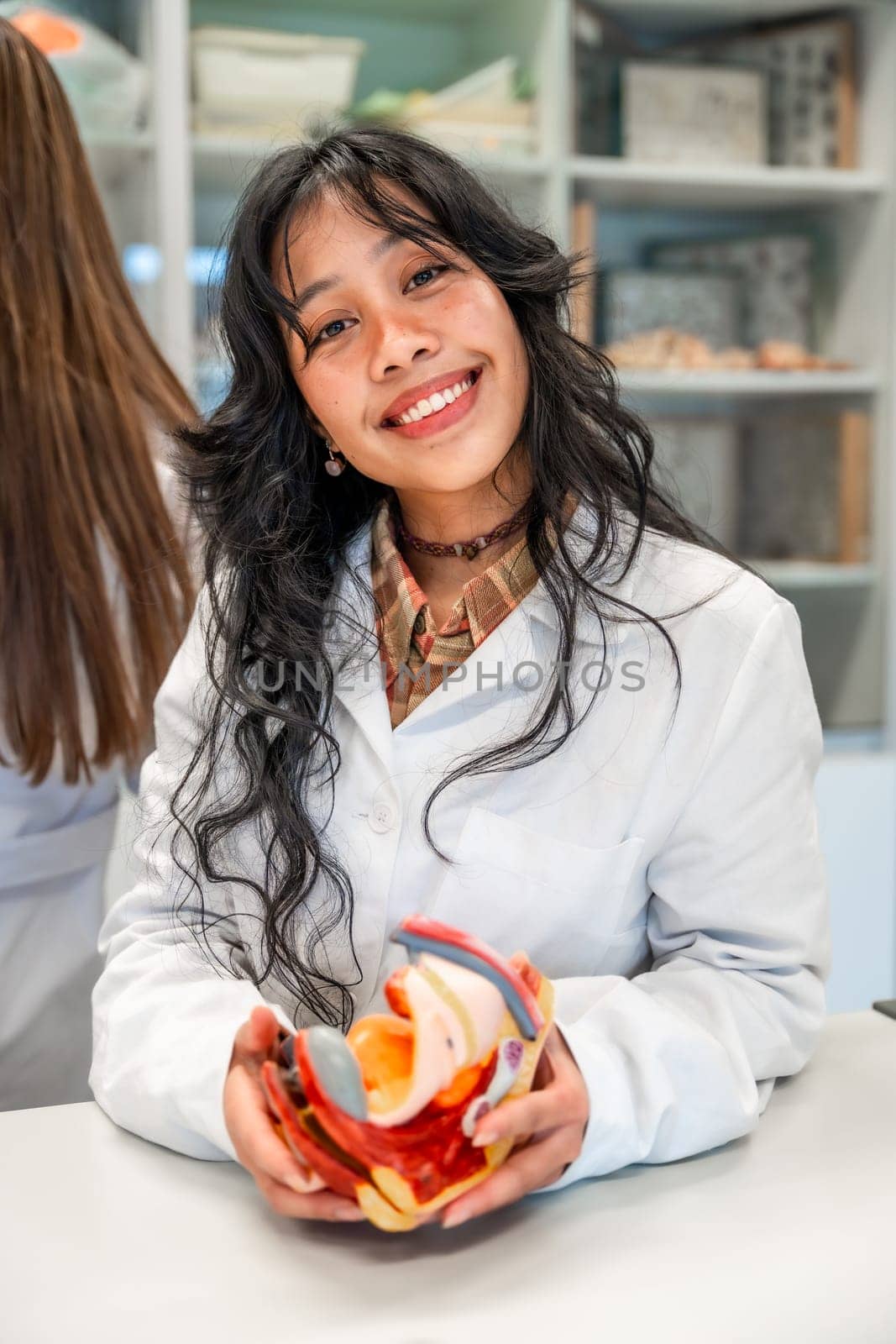 Smiling medical student holding anatomical model of female reproductive organs during anatomy class in university laboratory