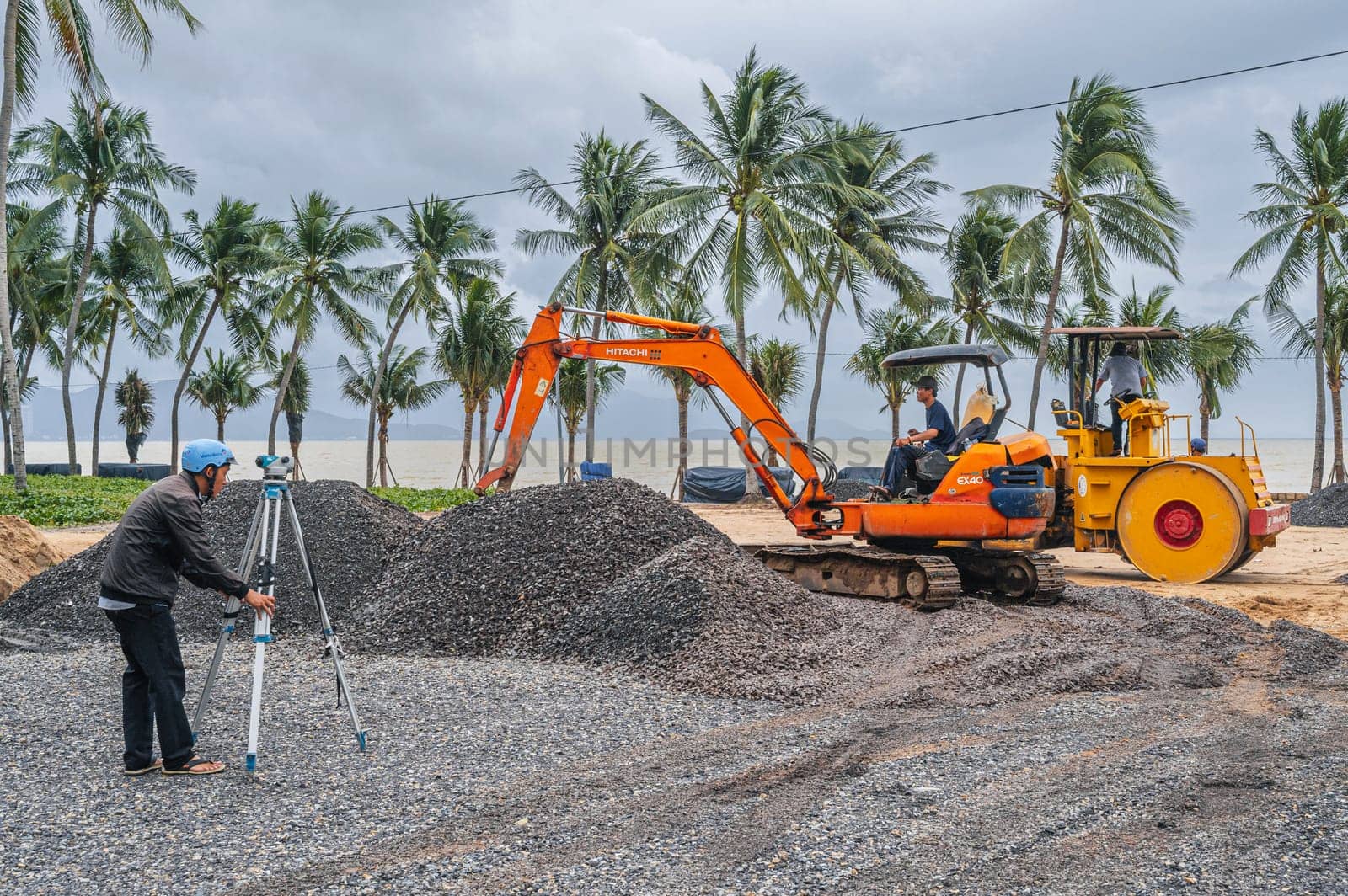 Construction heavy machinery excavator and builder with theodolite at a construction site on a beach by the sea in Asia. Nha Trang, Vietnam - December 14, 2024