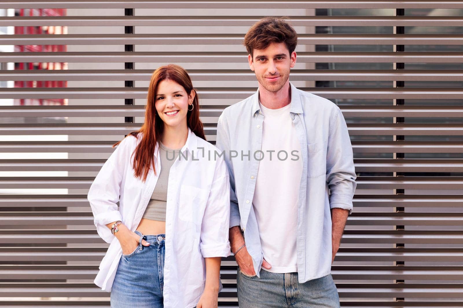 man and woman standing next to each other smiling looking at camera, both are wearing white shirt and jeans, they seem to be enjoying each other's company, concept of couple and urban lifestyle