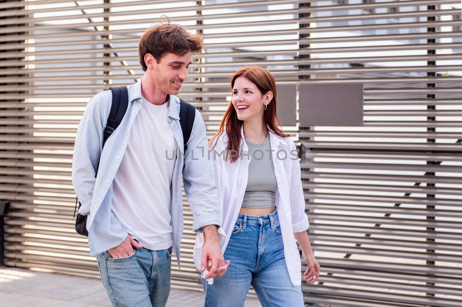 man and a woman walking together holding hands, the man is wearing backpack and jeans, while the woman is wearing white shirt and blue jeans, they seem to be enjoying each other's company