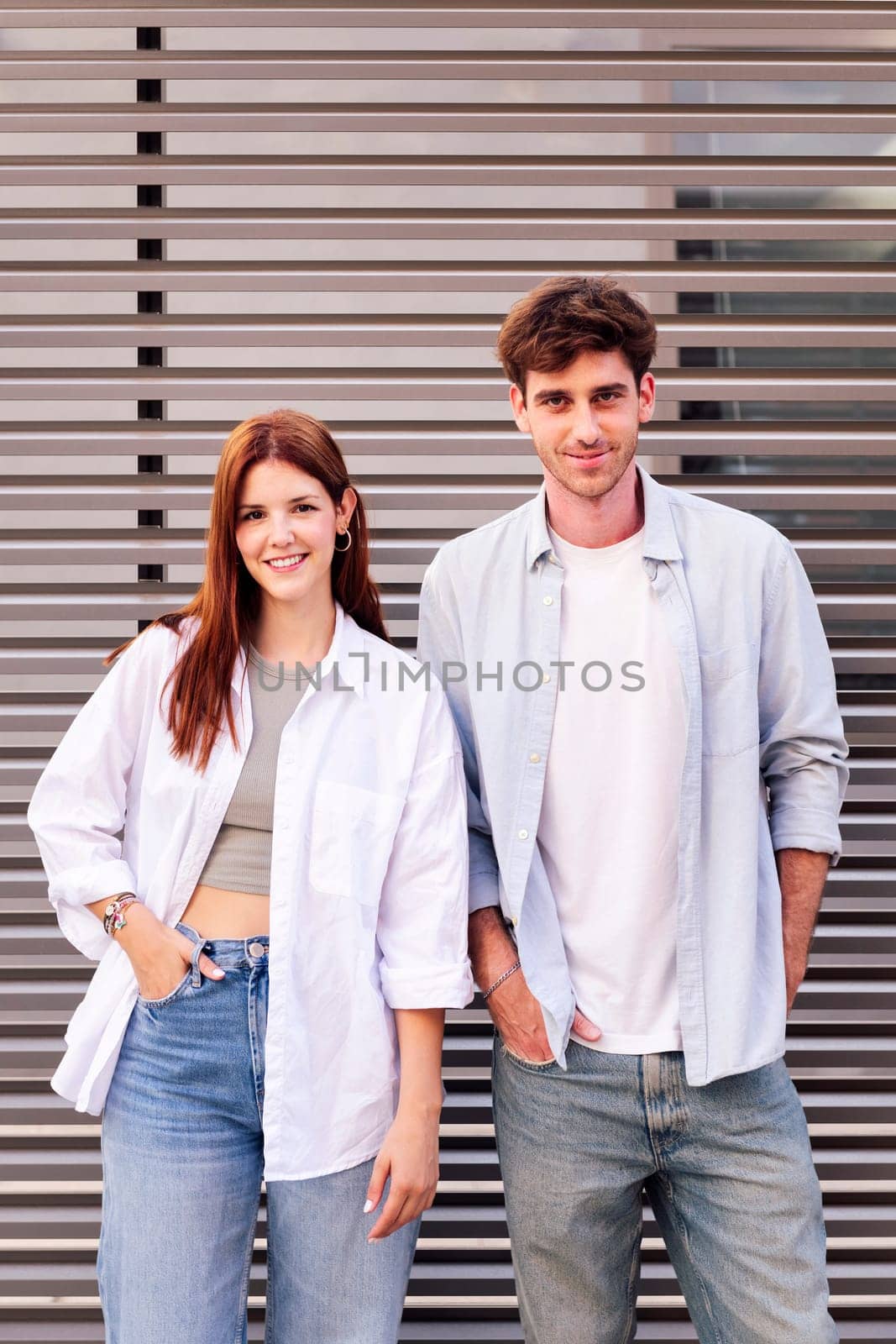 man and woman standing next to each other smiling looking at camera, both are wearing white shirt and jeans, they seem to be enjoying each other's company, concept of couple and urban lifestyle