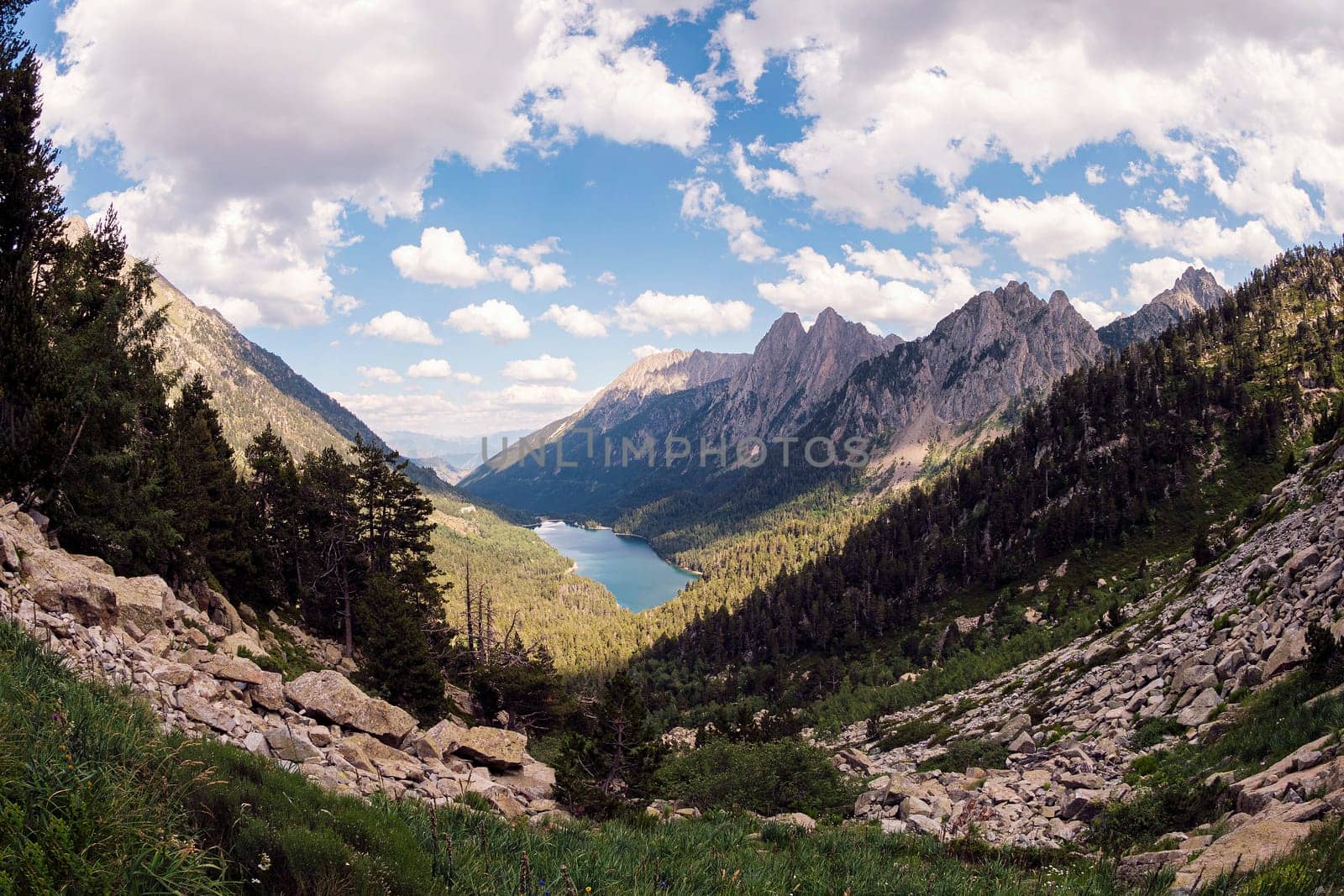 panoramic view of a mountain range with a lake in the valley, the sky is blue and the grass is green