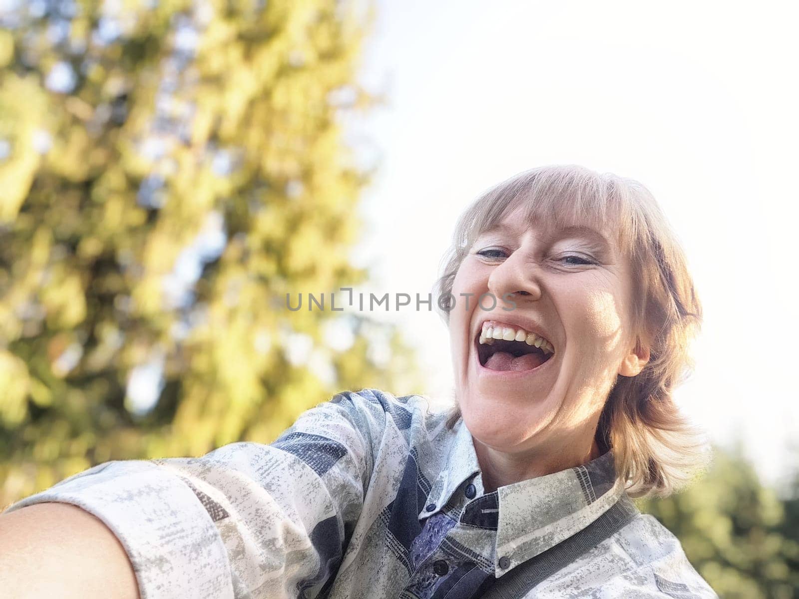 A cheerful middle-aged woman captures a lively selfie while exploring the beautiful outdoors on a sunny day.