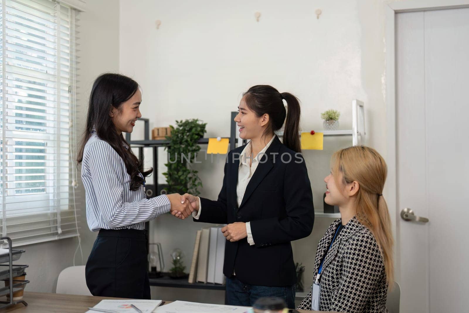 Two women shake hands in a positive meeting while another looks on, celebrating teamwork and success in financial planning.