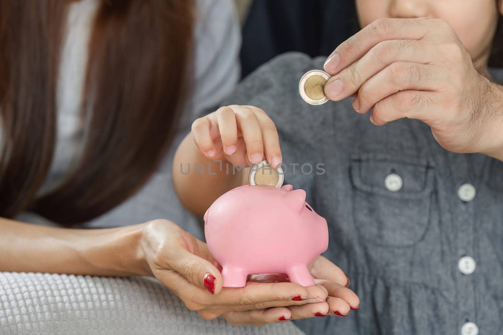 A family helps a child save coins in a piggy bank, emphasizing the importance of saving and financial responsibility.