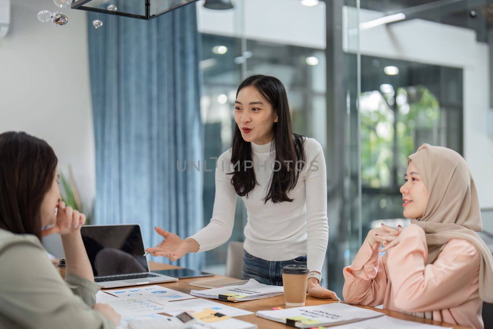 A group of diverse women engage in a productive meeting, sharing ideas and strategies in a contemporary office setting.