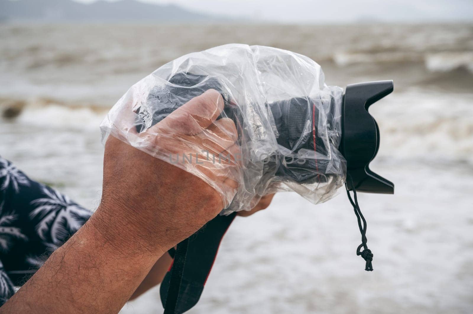 digital camera in waterproof case and a protective plastic bag against rain splashes in male hands of a photographer