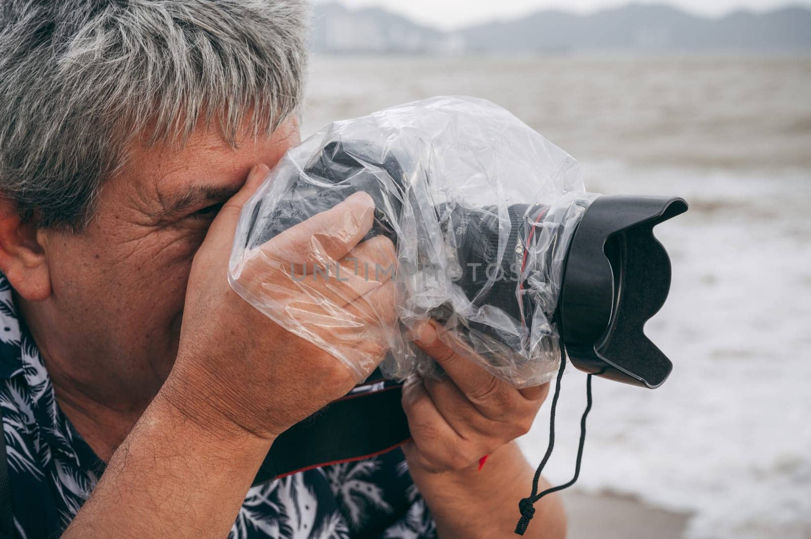 professional male photographer takes pictures with digital camera in a protective case and a waterproof plastic bag against splashing rain in nature