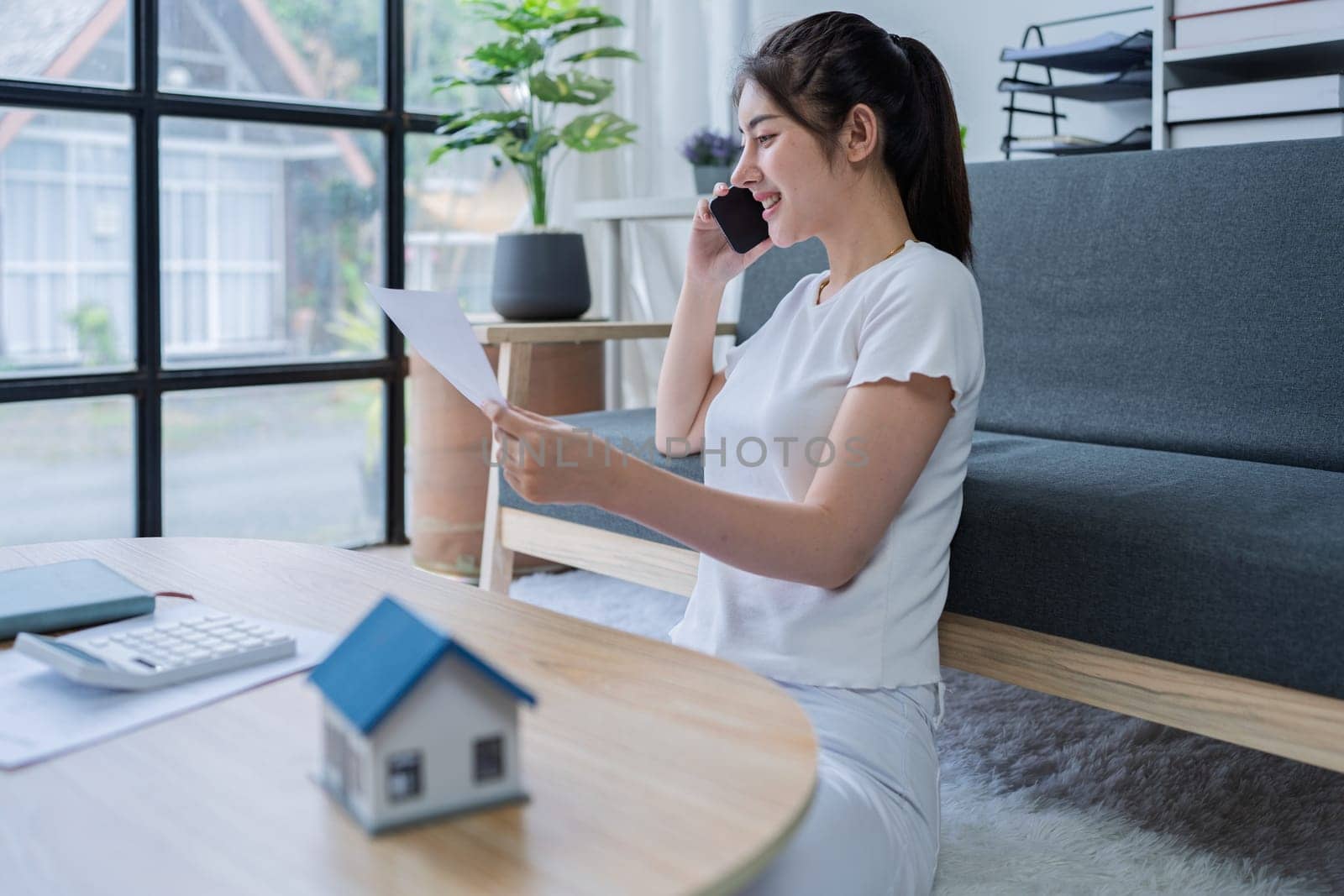 Young woman engaged in a phone conversation while working on home finances in a cozy modern living room.