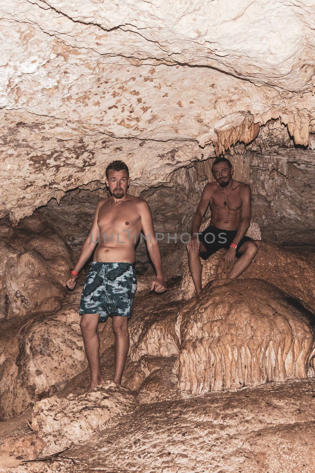 Mean male tourists friends are posing and climbing in the turquoise green blue water and rocks in cenote Yaxmulito in Tulum Quintana Roo Mexico.