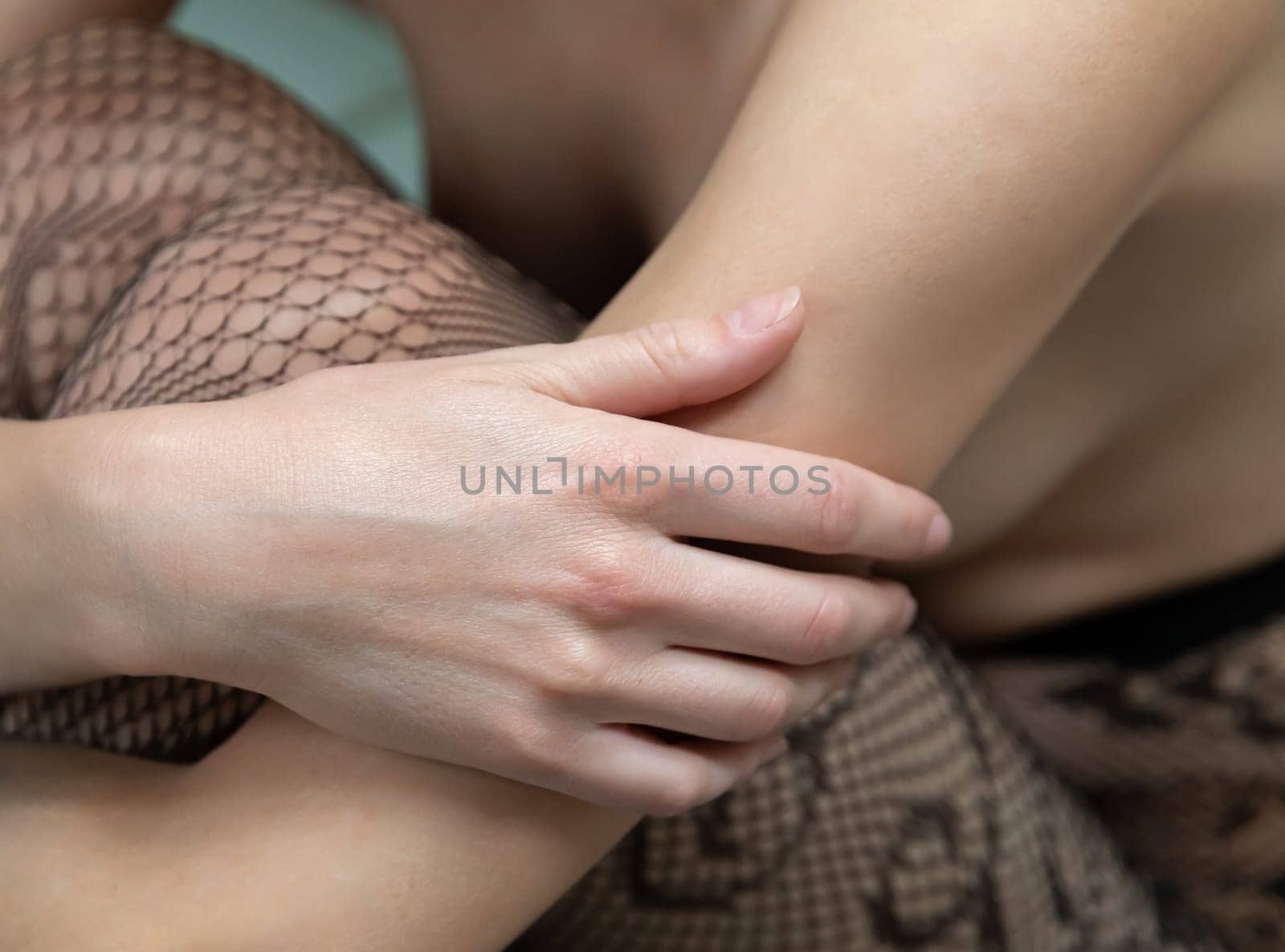 Soft hands are gently resting on the legs, adorned with intricate fishnet stockings. The focus is on skin textures and textiles, creating a tranquil and intimate atmosphere.