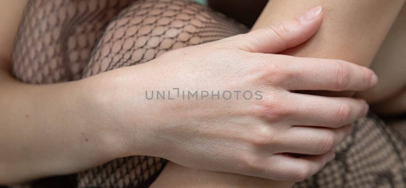 A hand gently rests on a bare leg adorned in fishnet stockings, capturing a moment of relaxation and intimacy. The setting suggests comfort and a peaceful atmosphere.