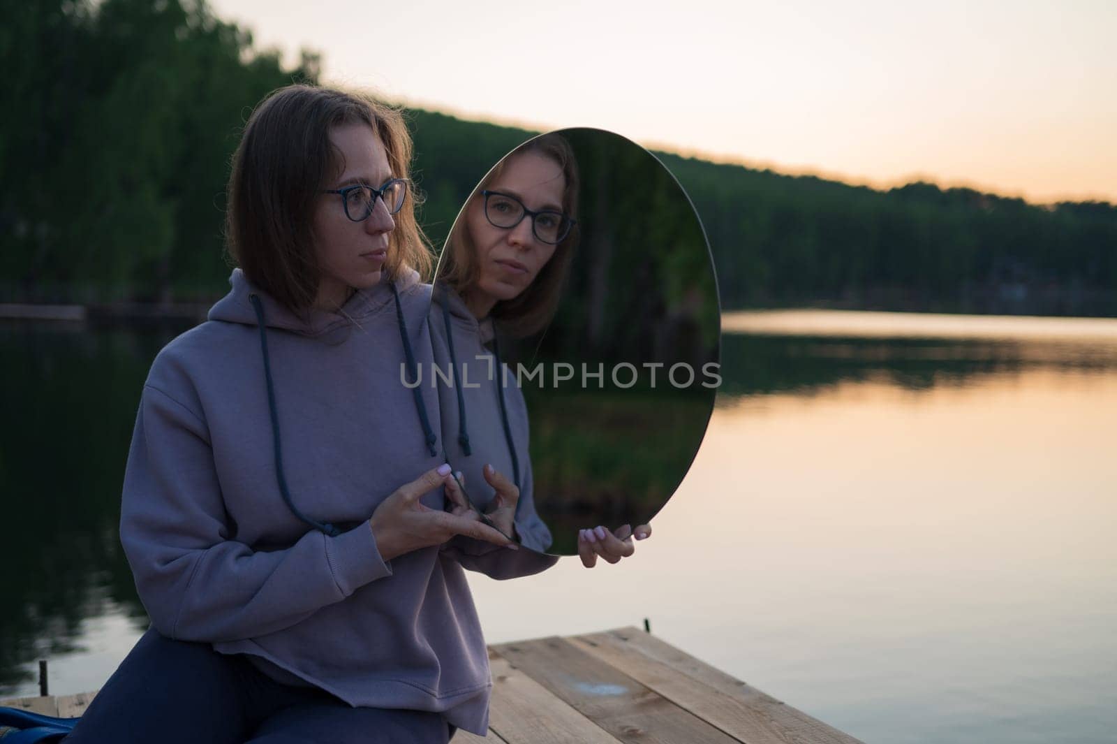 Woman with mirror on the pier at lake, closeup portrait, summer sunset
