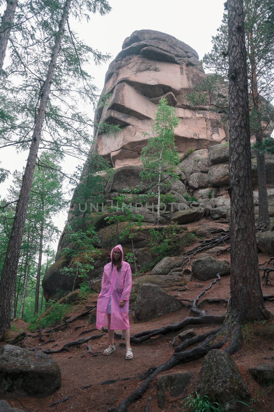 Woman in raincoat in the taiga forest and rocks of the Stolby nature reserve park, Krasnoyarsk, Russia