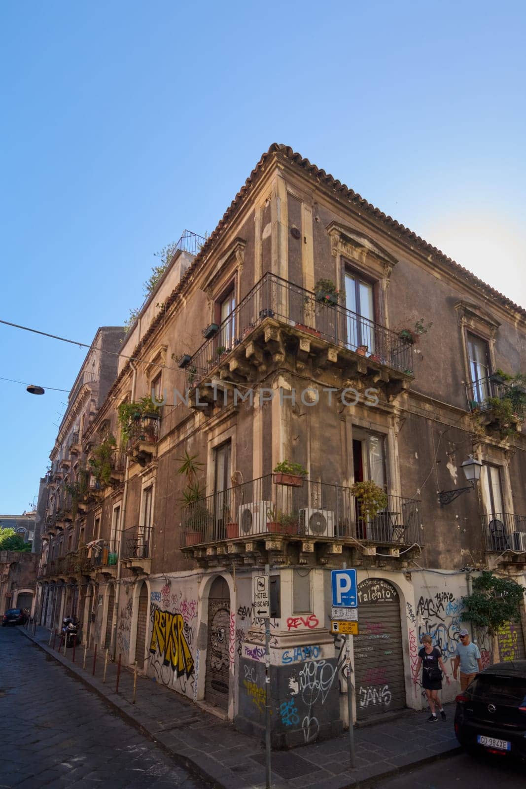 Catania, Italy - February 25, 2025: Narrow Catania alley showcases historic buildings, graffiti, and greenery, bathed in sunlight in Sicily. Concept: Rustic city charm
