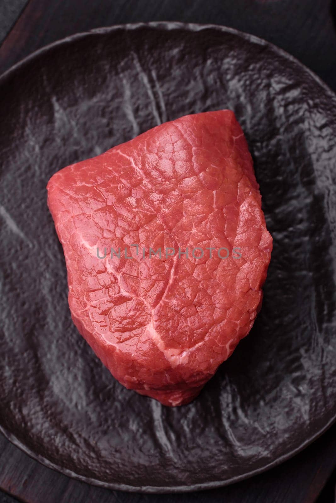 Raw beef tenderloin ribeye steak with salt and spices on a dark concrete background