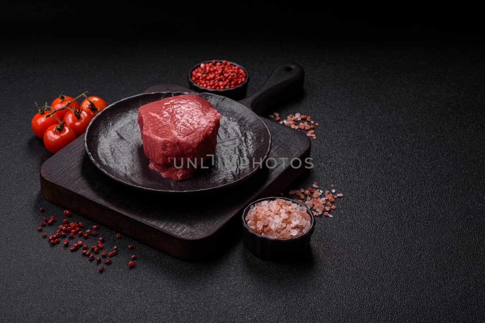 Raw beef tenderloin ribeye steak with salt and spices on a dark concrete background