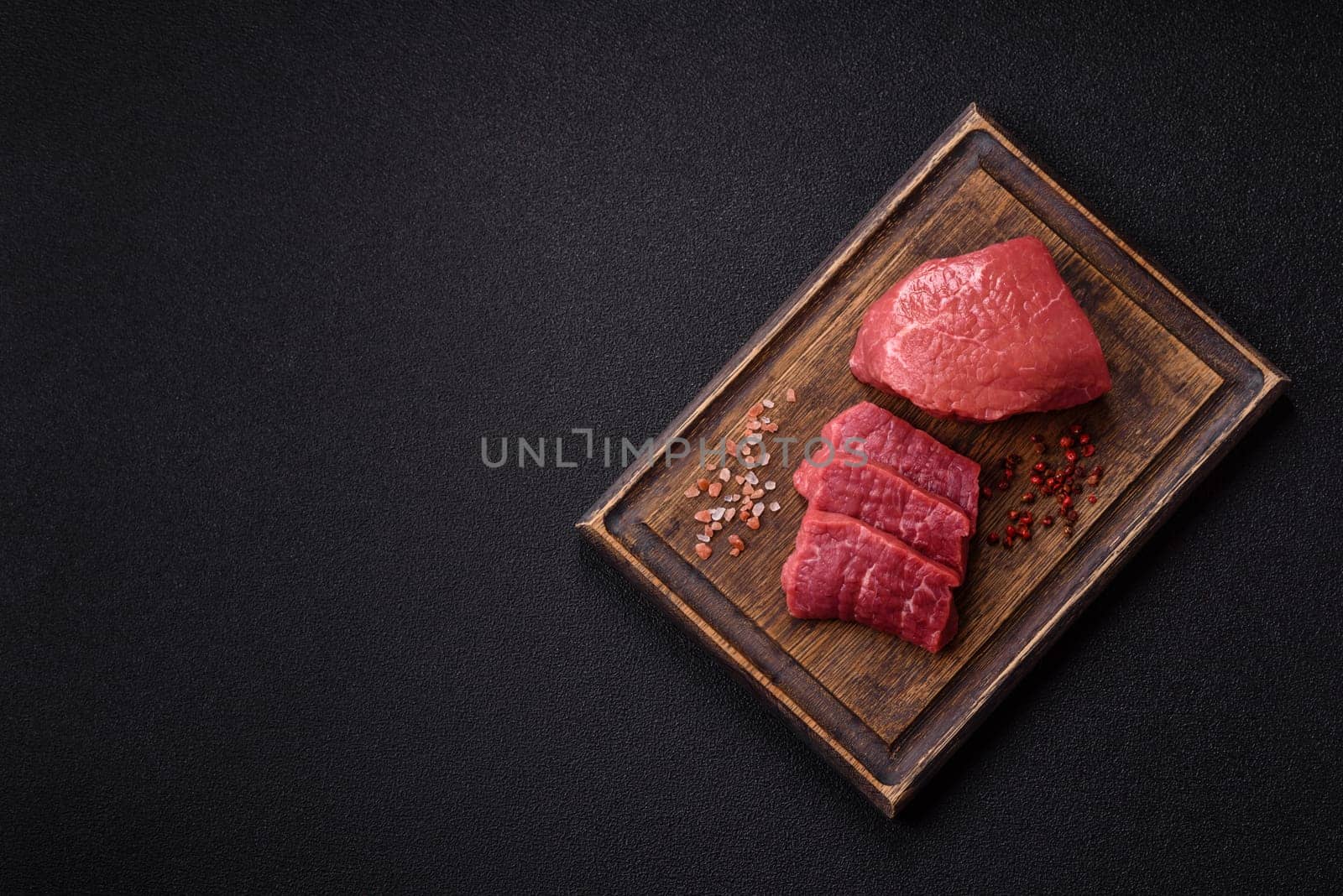 Raw beef tenderloin ribeye steak with salt and spices on a dark concrete background