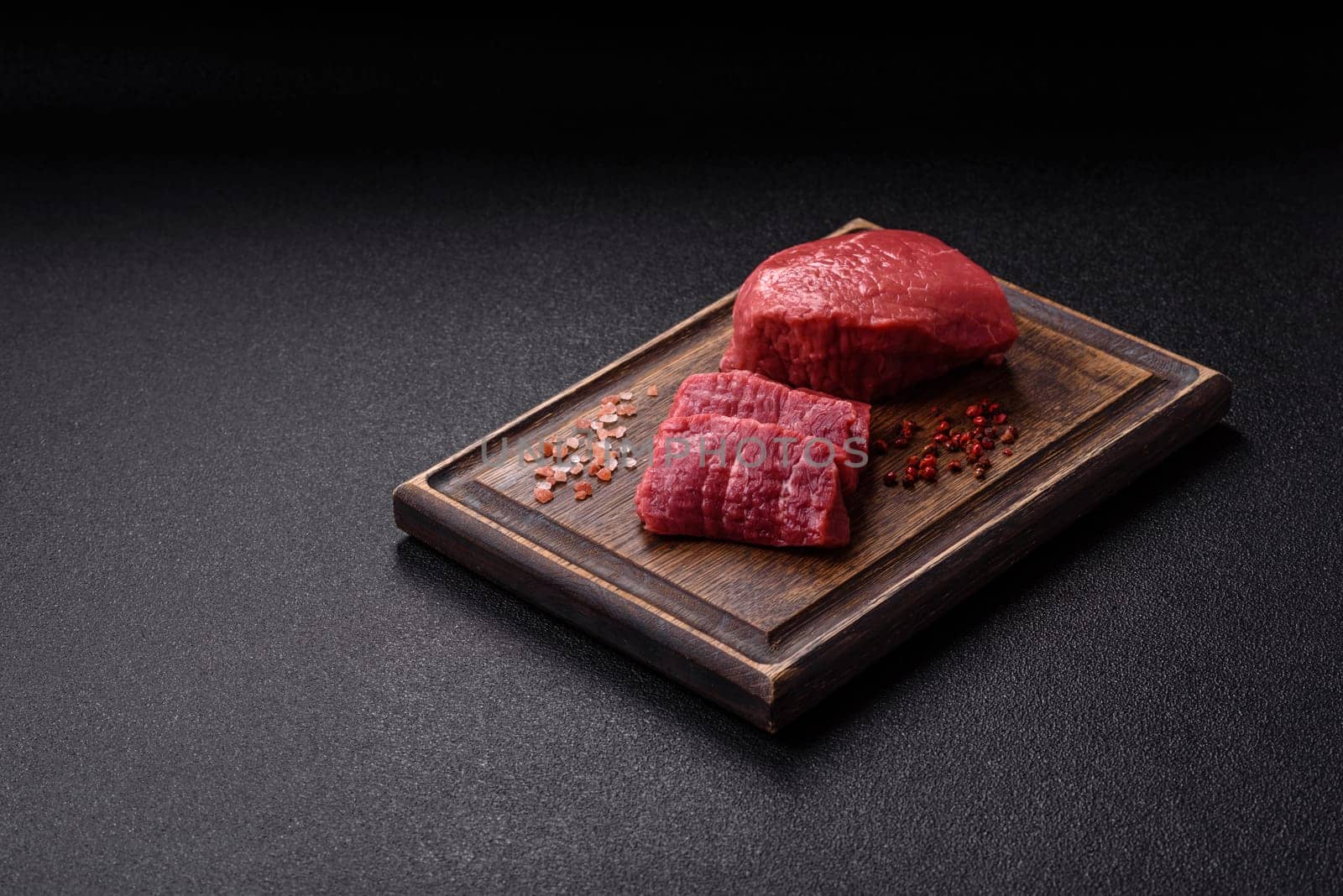 Raw beef tenderloin ribeye steak with salt and spices on a dark concrete background