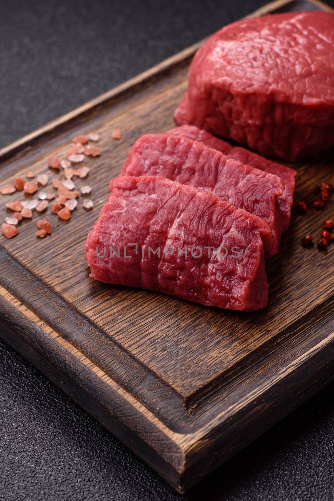 Raw beef tenderloin ribeye steak with salt and spices on a dark concrete background