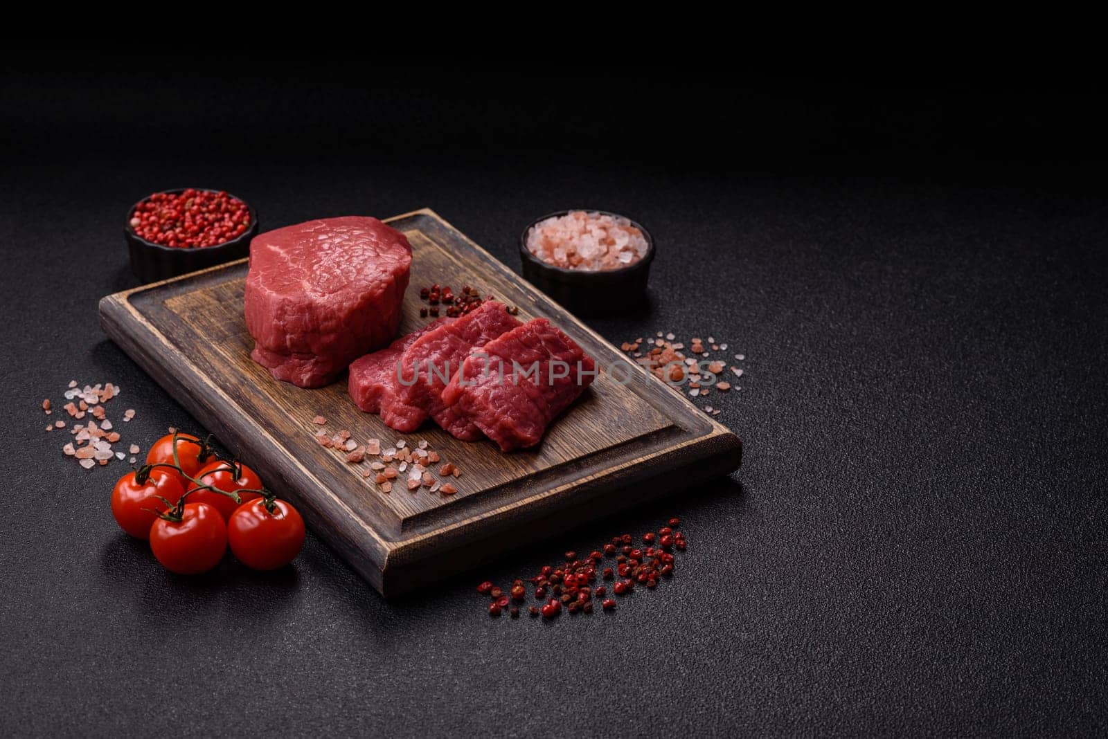 Raw beef tenderloin ribeye steak with salt and spices on a dark concrete background
