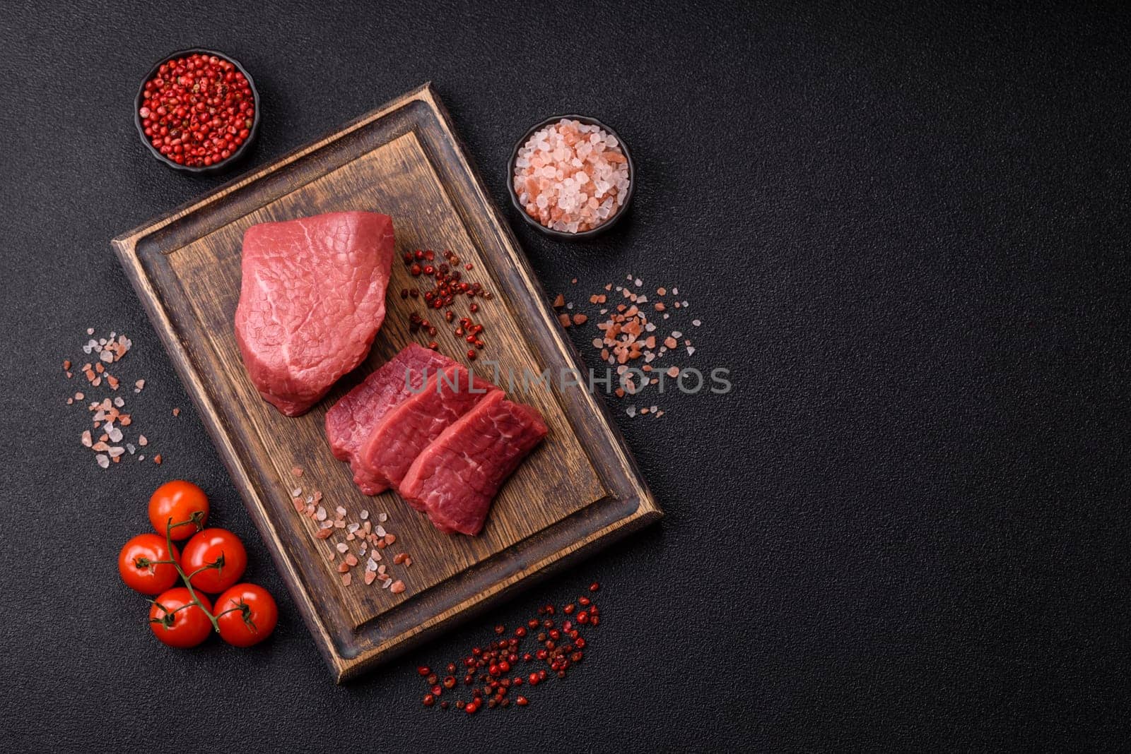 Raw beef tenderloin ribeye steak with salt and spices on a dark concrete background