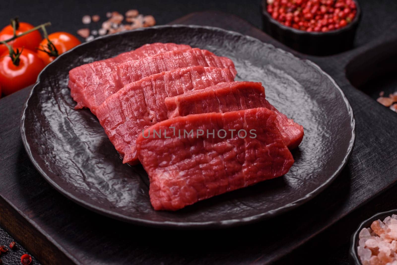 Raw beef tenderloin cut into slices with salt and spices on a dark concrete background