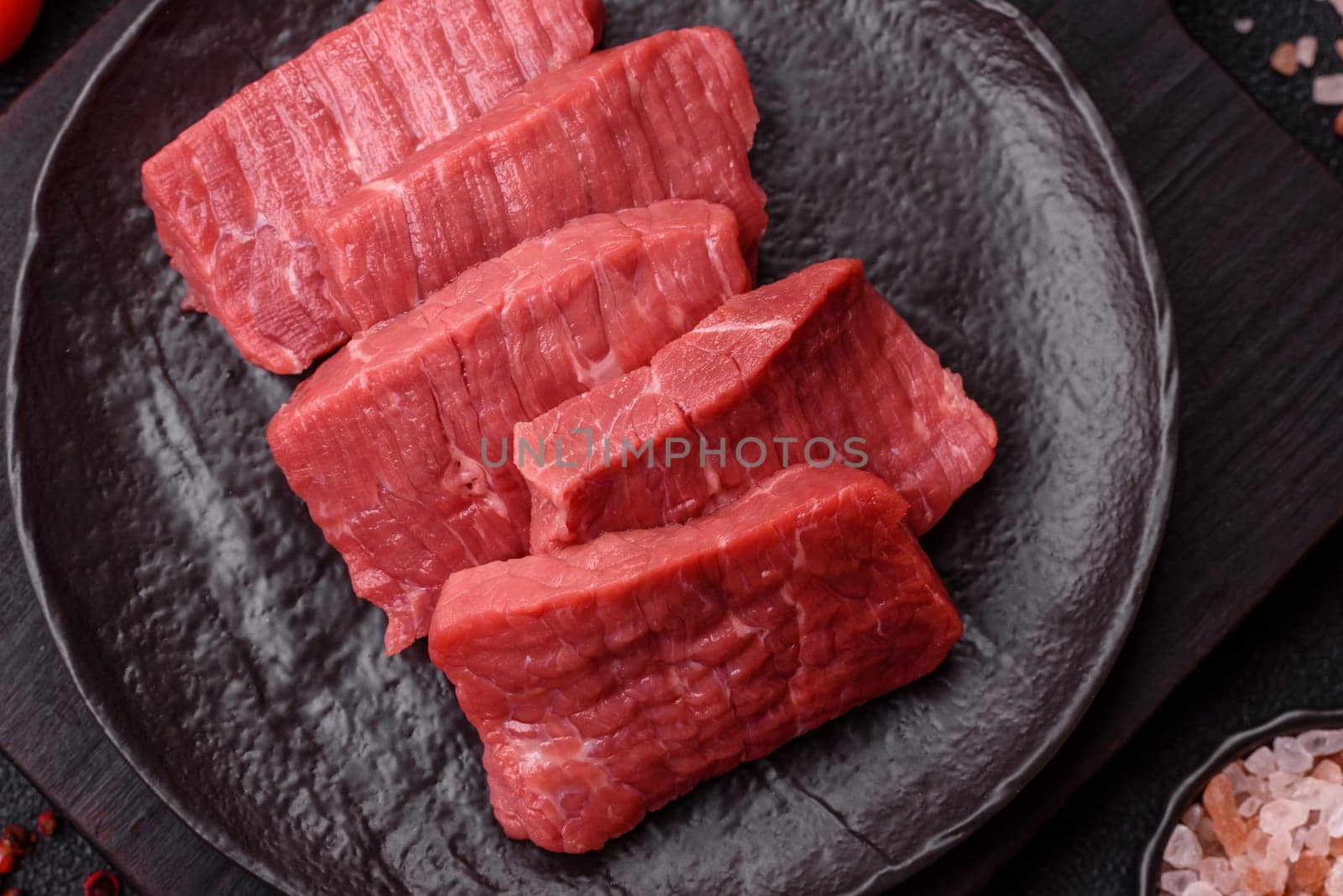 Raw beef tenderloin cut into slices with salt and spices on a dark concrete background