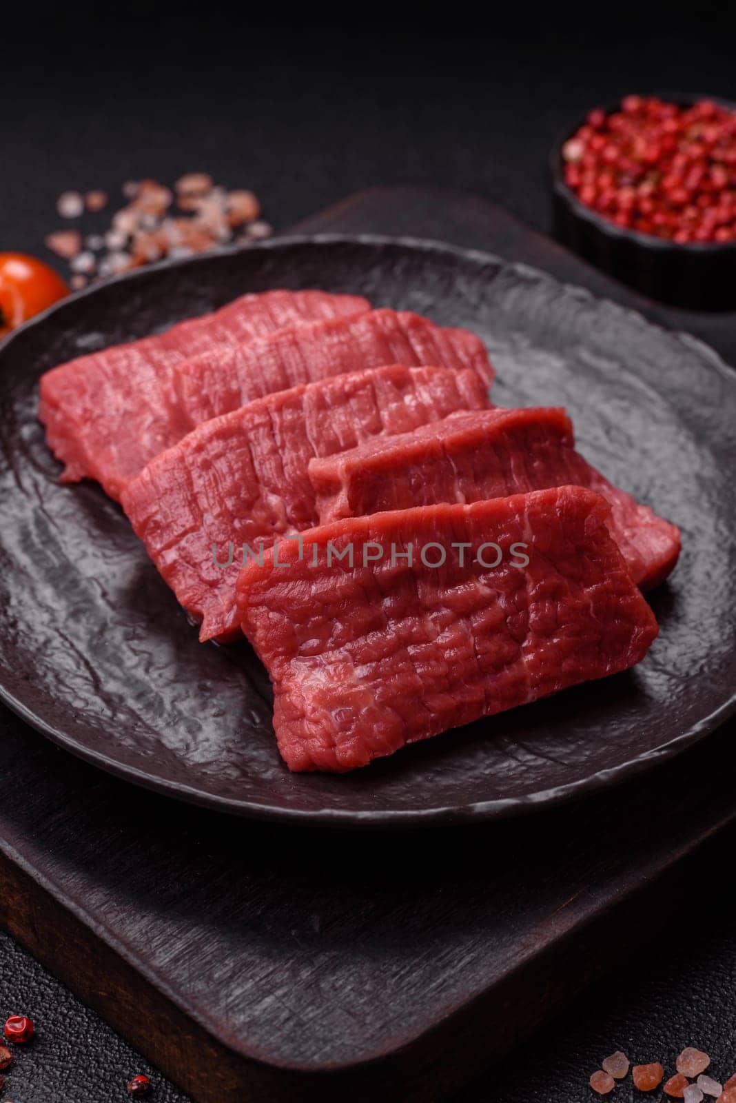 Raw beef tenderloin cut into slices with salt and spices on a dark concrete background