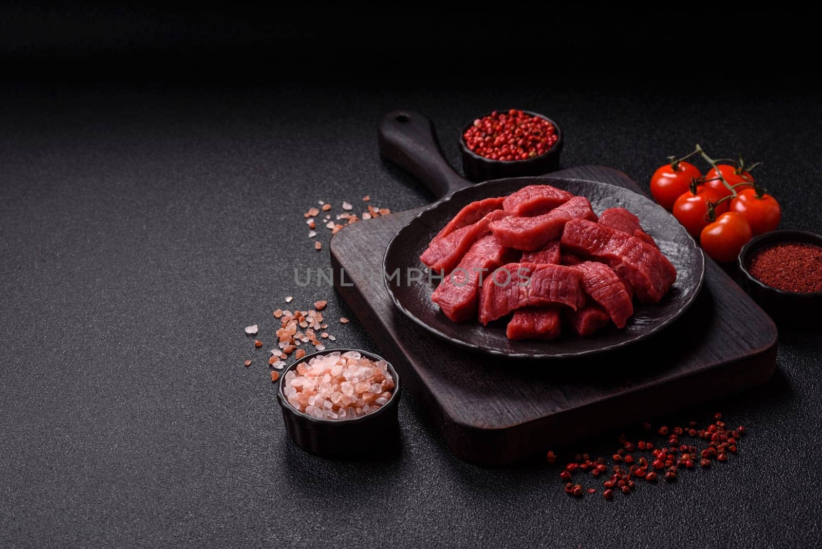 Raw beef tenderloin cut into slices with salt and spices on a dark concrete background